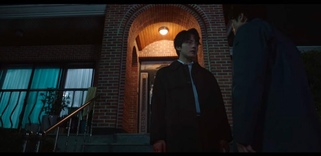 Joo-won stands outside a crime scene being confronted by Dong-shik. He is back lit by a porch light.