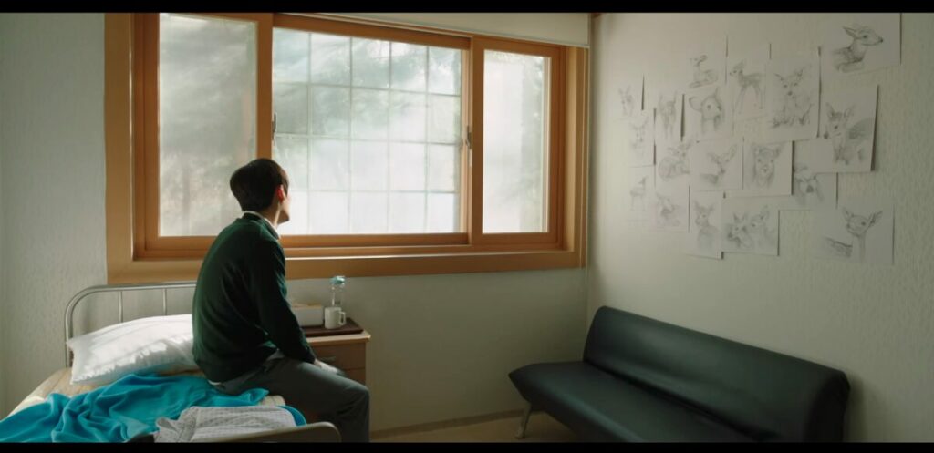 Park Jung-jae sits ion a metal single bed n a mental hospital, highly medicated, and staring blankly out the window. In front of him, the wall is plastered with his drawings of fawns.