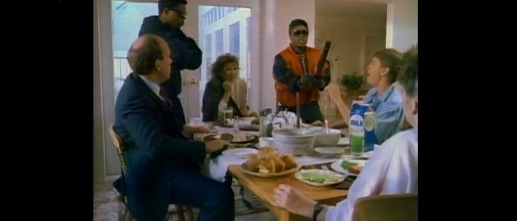 A white suburban family sits around a laden breakfast table while black thugs threaten them with sawn off shot guns