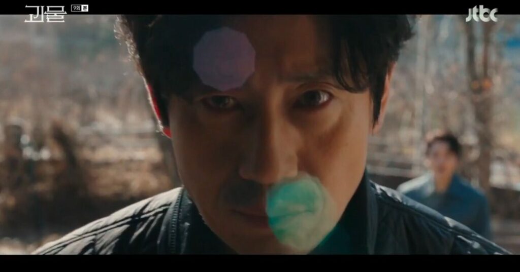 Dong-shik in one of the show's now-famous fourth-wall breaks. He's in close up staring at us through the camera bathed in morning light with lens flare on his face and Joo-woon small and blurred in the background