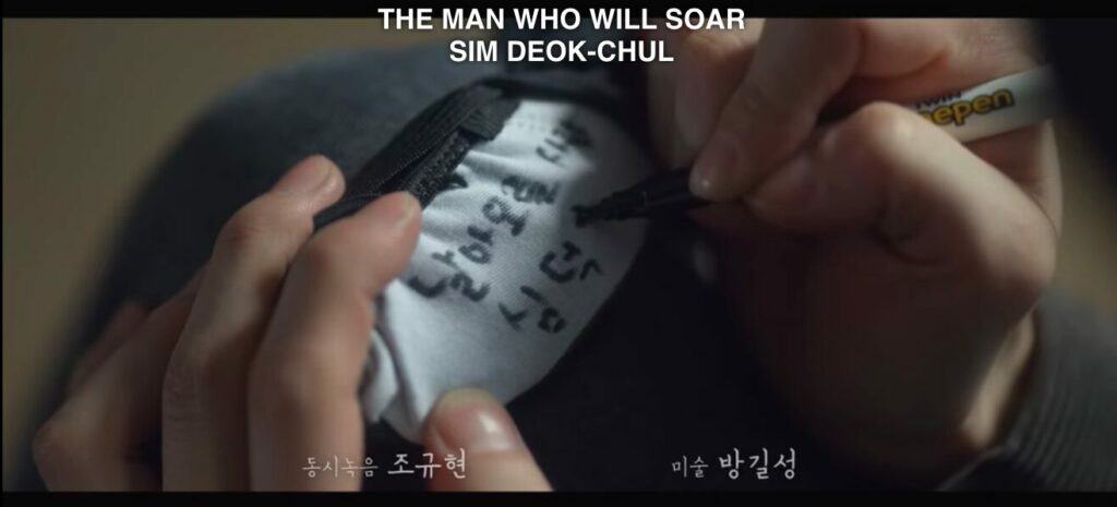 Chae-rok's fingers writing on the bottom of Deok-chul's shoes, "The man who will soar"