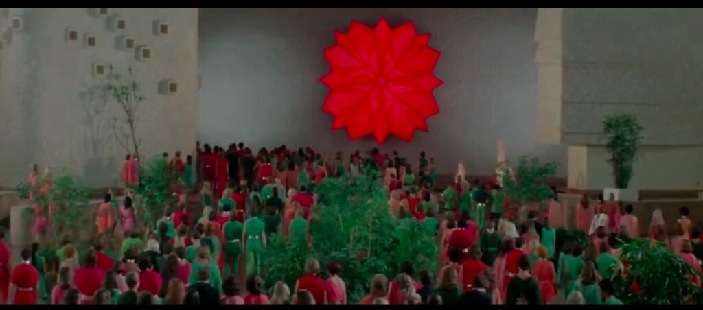The citizens walk en-masse in reds and greens toward the Carousel Room