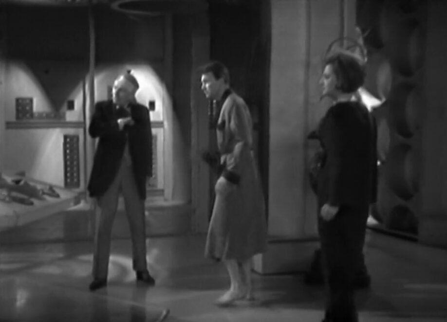 The Doctor with a head injury, Ian in a dressing gown and Barbara look with concern at the TARDIS' central column.