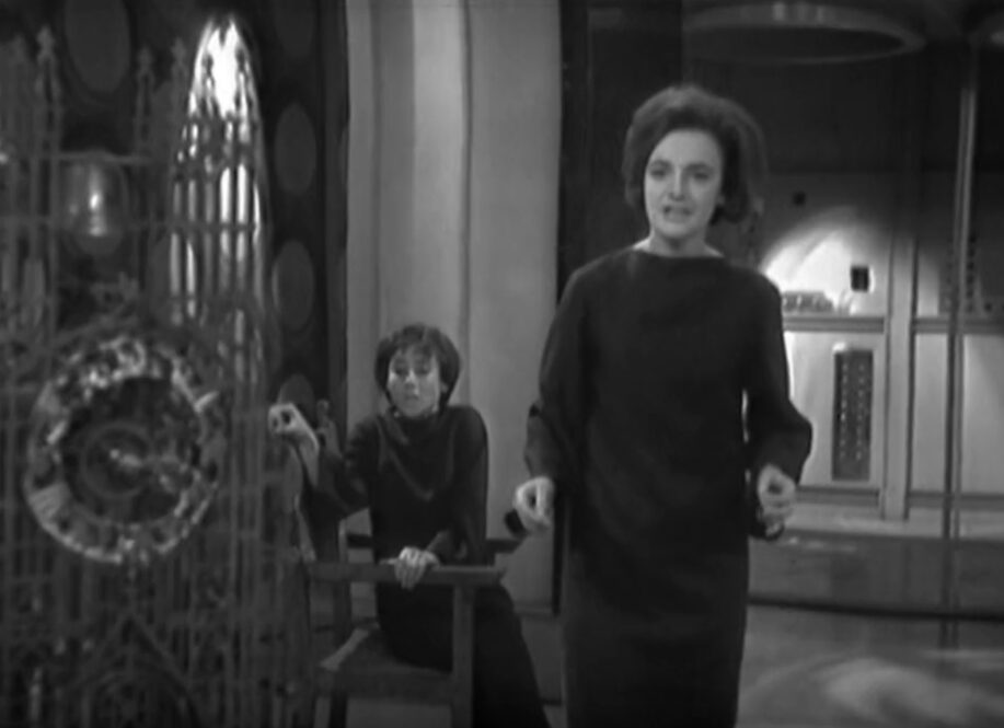 Barbara approaches a clock while Susan looks on, scared