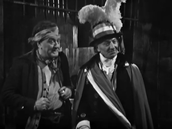 The Doctor dressed as a regional officer with a huge feather in his hate talks to a jailor.