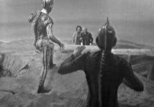 Reptile aliens in the foreground loom menacingly over Barbara and the Doctor over the next dune.
