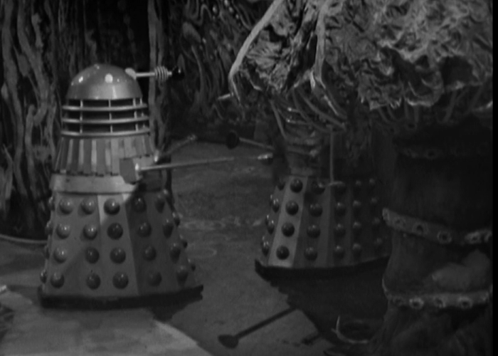 A Dalek looks on while another Dalek is swallowed by a giant carnivorous fungus.