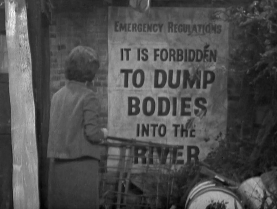 Barbara stands in horror reading the sign about it being forbidden to dump bodies into the river