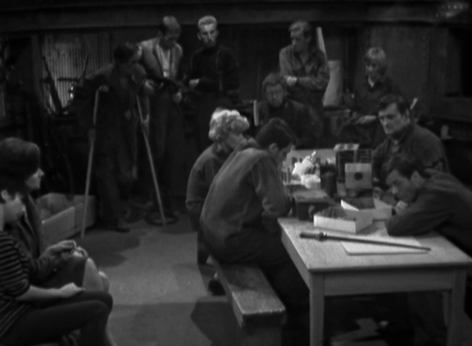 Members of the Resistance sit around making plans on a table and listening to a radio and in an underground room