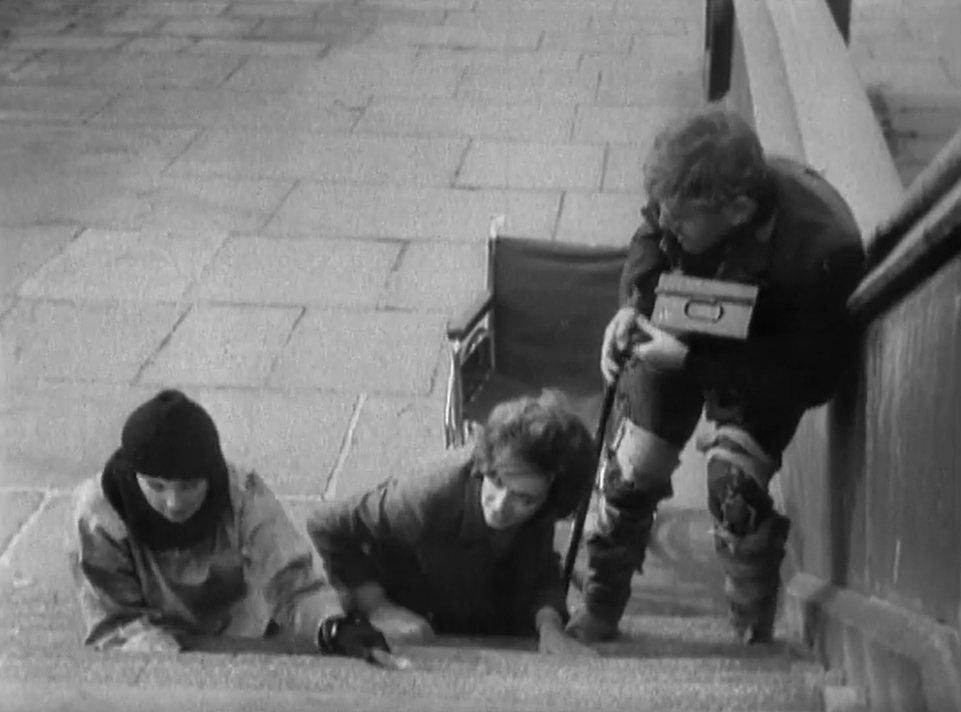 Barbara and resistance fighter, Jenny crawl up a set of stairs near Embankment in London along with Dortmun who's had to leave his wheelchair and try to get up the stairs by his own efforts.