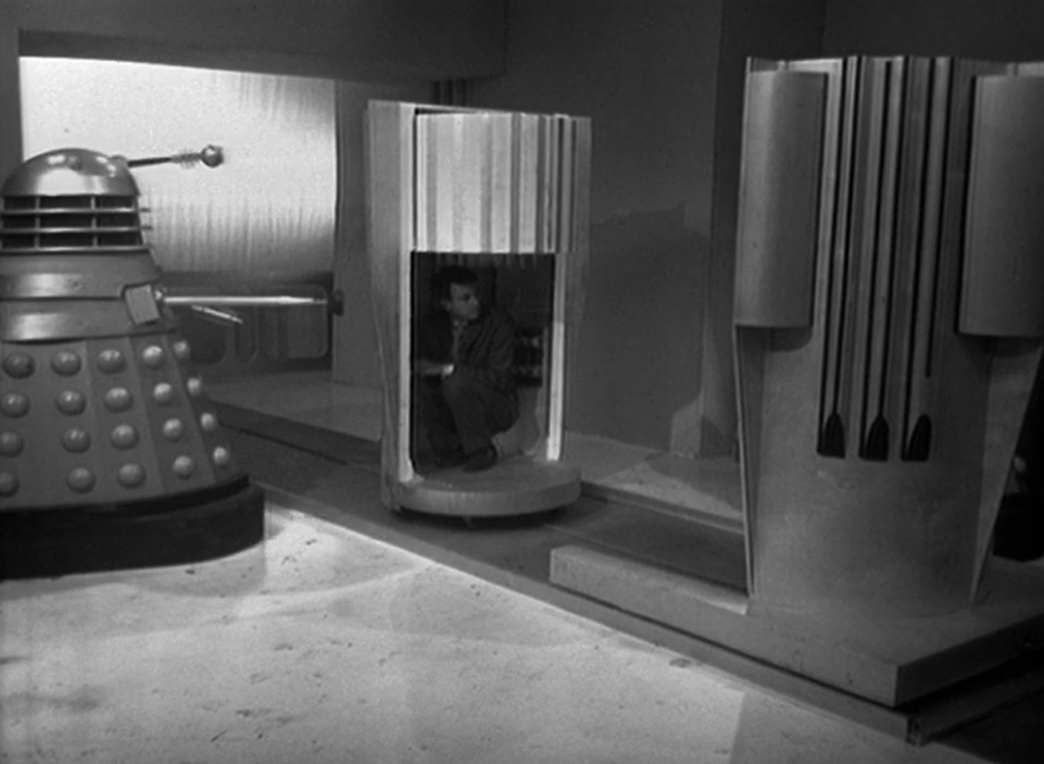 Ian crouches in a metal tube to hide from a nearby Dalek, unaware it is a bomb