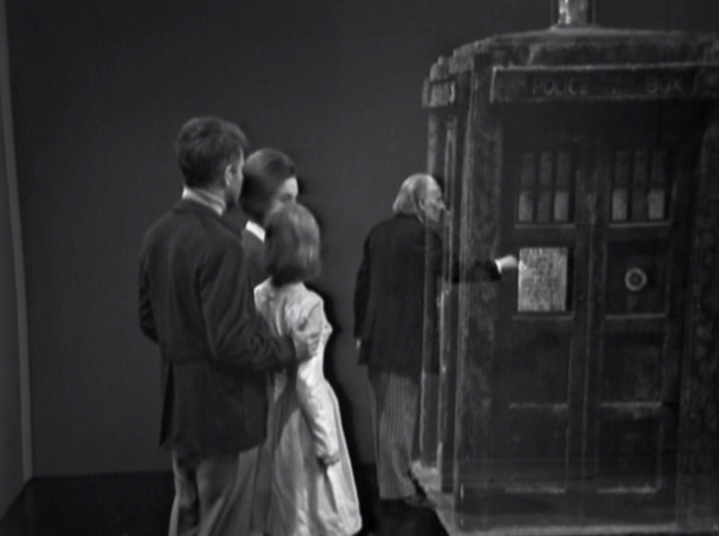 Ian, Barbara and Vicki look on while the Doctor tries to open the TARDIS door and has his hand go right through it.