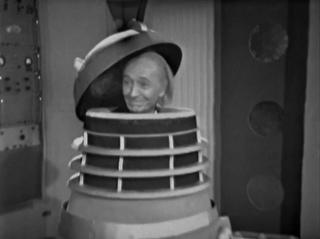 The Doctor pops his head out of a Dalek casing with an impish grin on his face