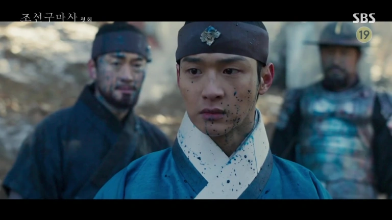 Jang Dong-yoon dressed as a King in a Sageuk splattered in what appears to be blue blood. Behind him are two guards equally covered in the same blood.